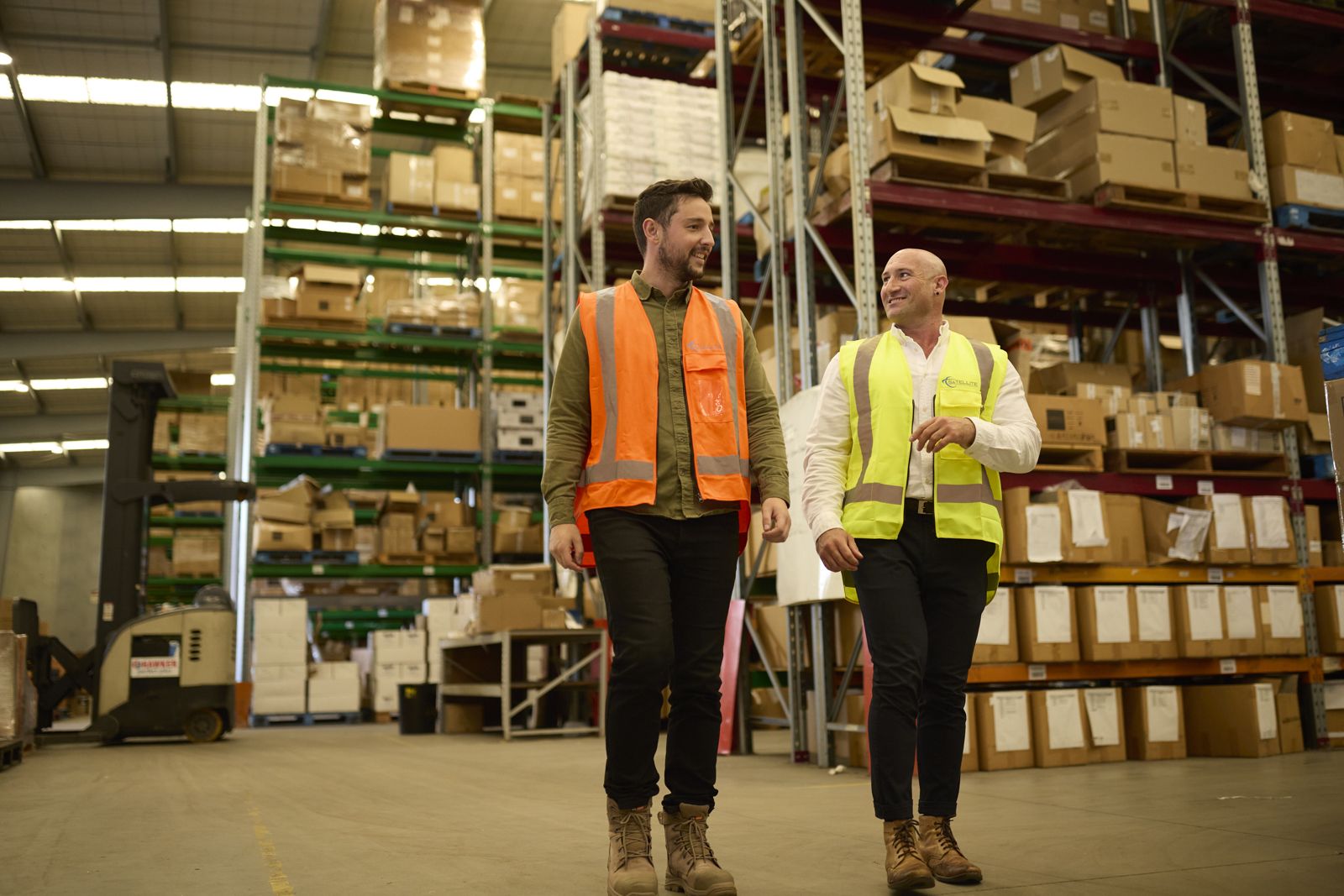 Two Satellite3PL team members walking between stocked pallet racking in the Māngere warehouse